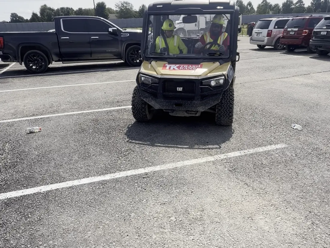 A site vehicle working a commercial parking lot between parked cars.