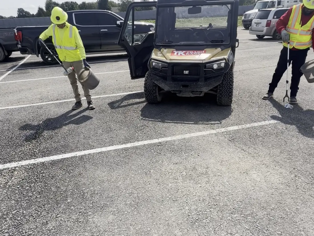 Crew clearing litter across a large lot with the site vehicle alongside.
