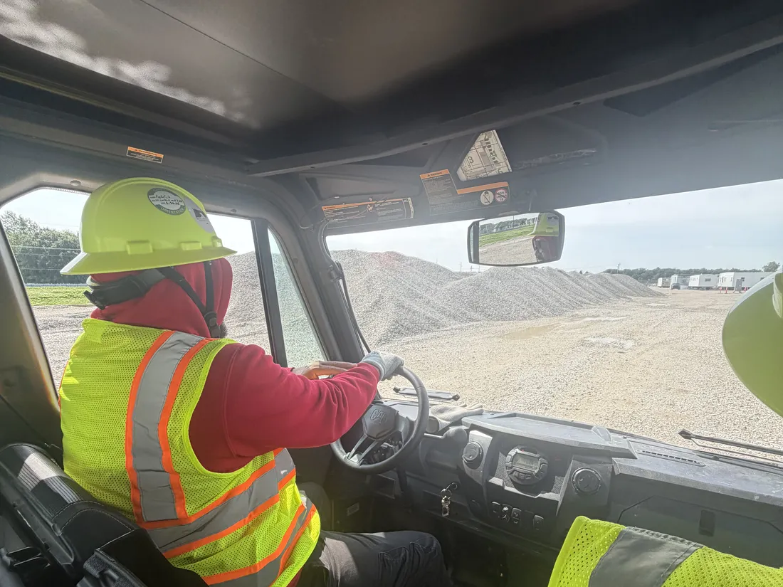 A Star City Environmental operator in a hard hat and high visibility vest driving a site vehicle across a gravel site.