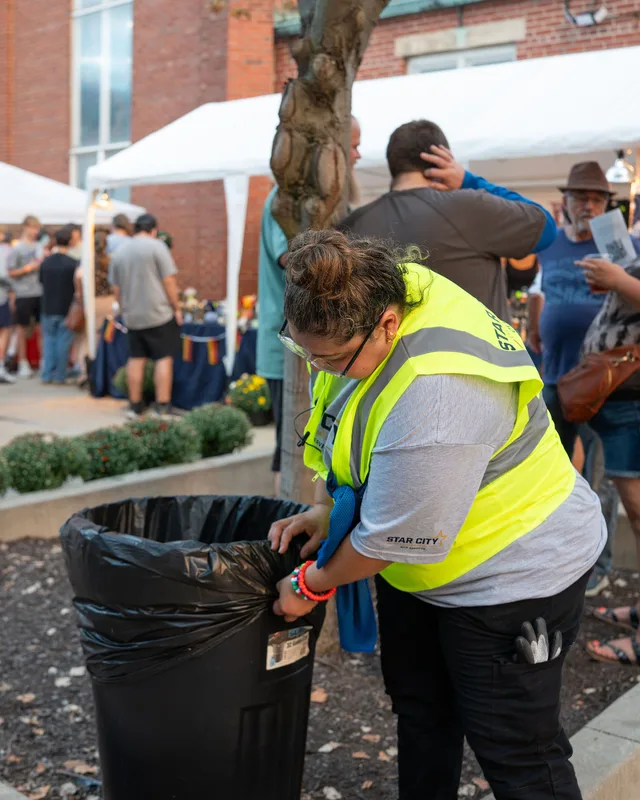 A crew member bagging waste from a bin at a street festival.