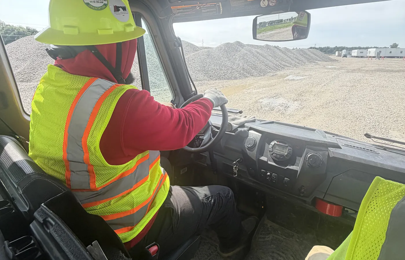 An operator at the wheel of a site vehicle looking out across a gravel site.