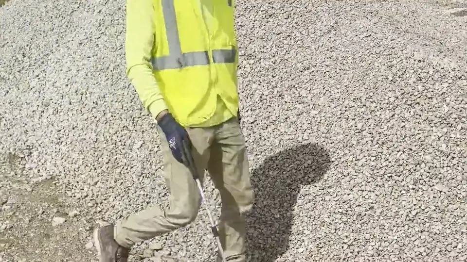 A crew member collecting debris from a gravel area with a grabber.