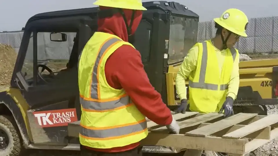 Two crew members loading material into the bed of a site vehicle.