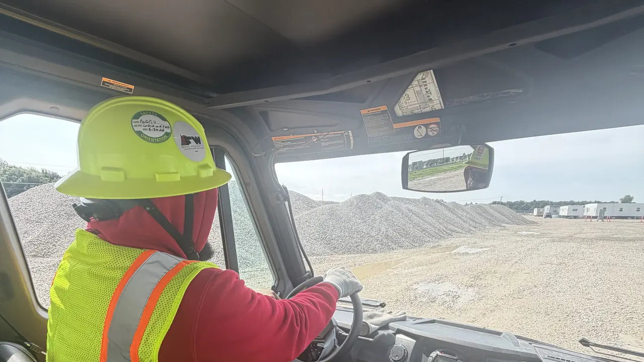 An operator in a hard hat and high visibility vest at the wheel of a site vehicle.