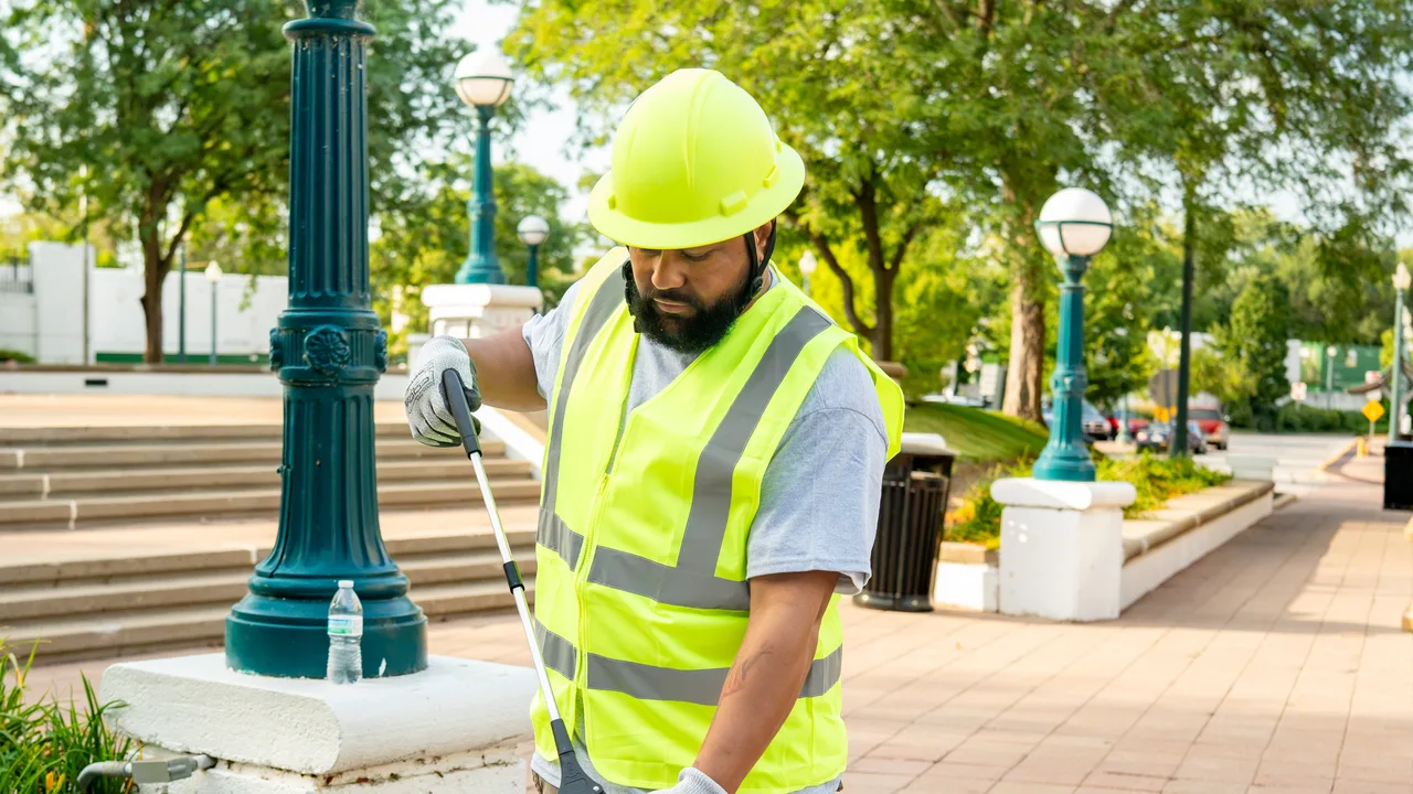 A crew member using a litter grabber across a commercial plaza.